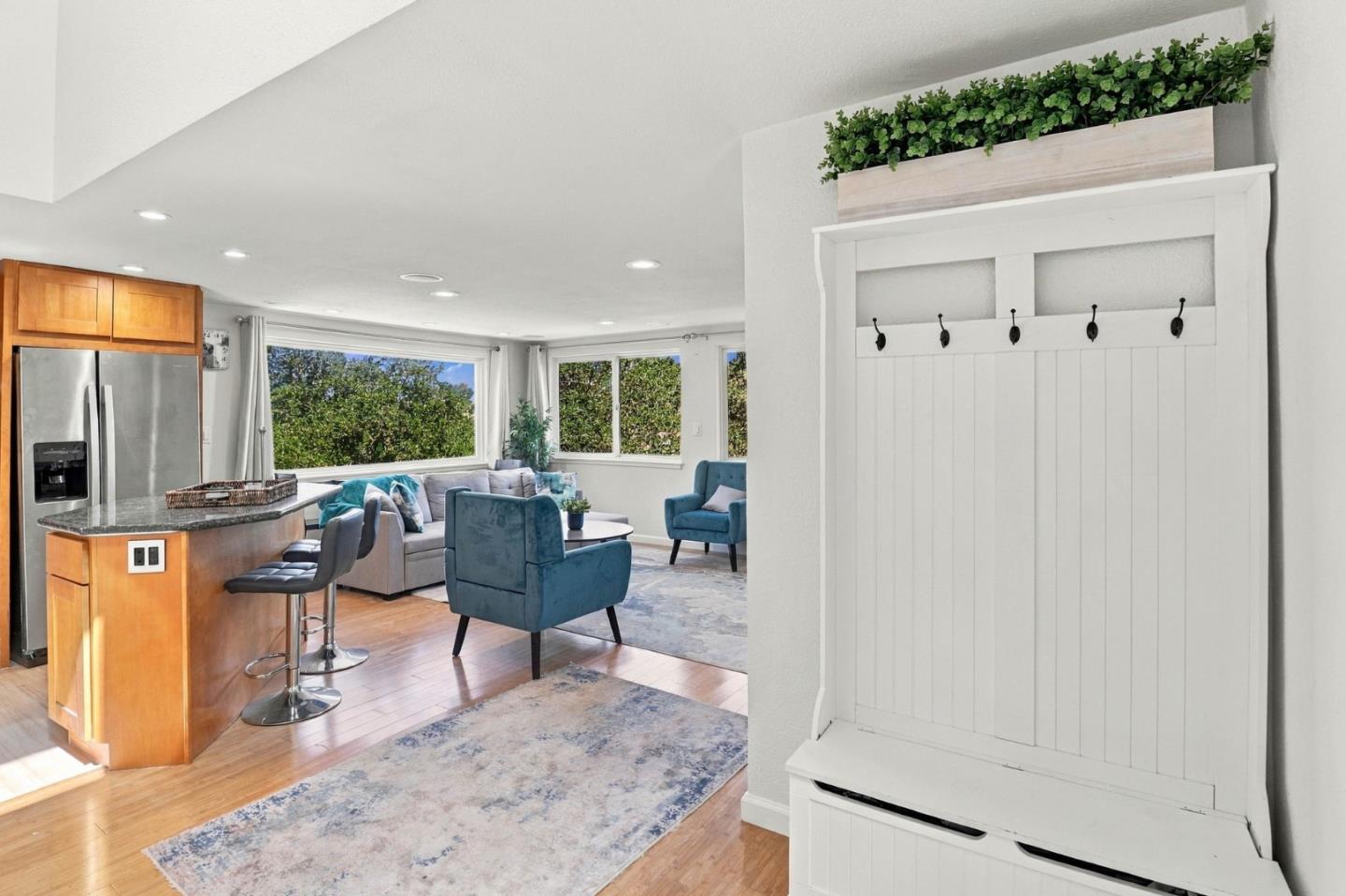 Open-plan living room and kitchen with blue chairs, large windows, and a built-in white entry bench.