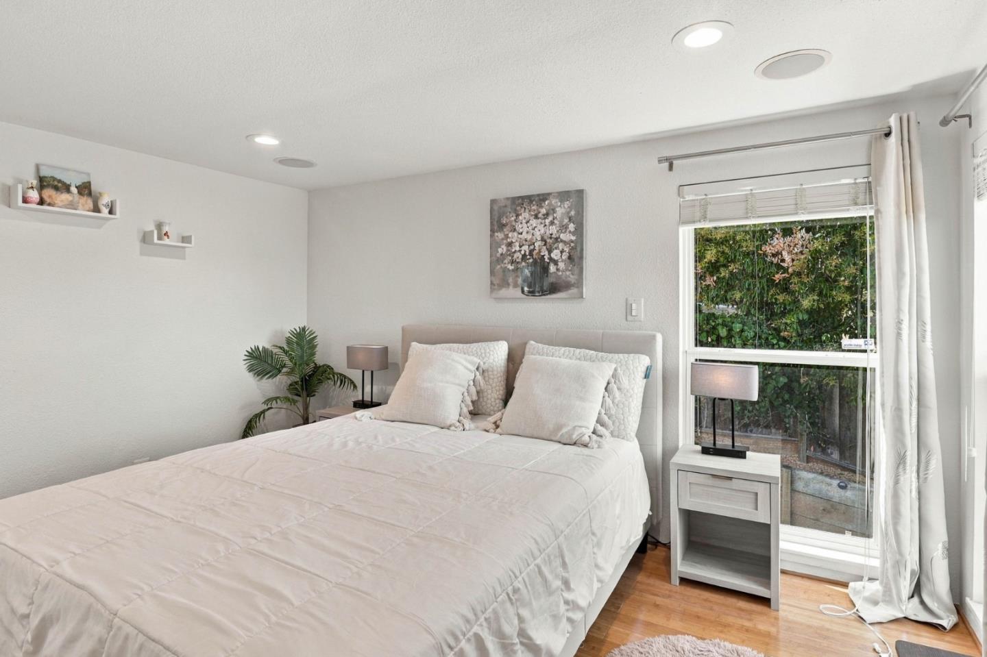 Bedroom with a white bed beside a large window overlooking greenery.
