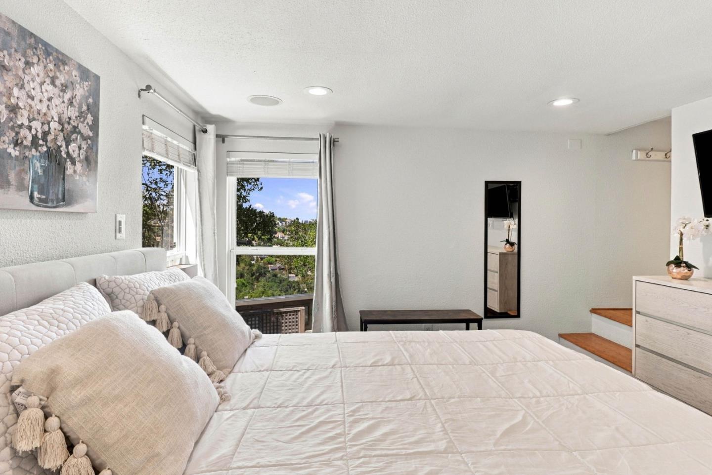 Bedroom with a white bed and windows overlooking a green hillside.