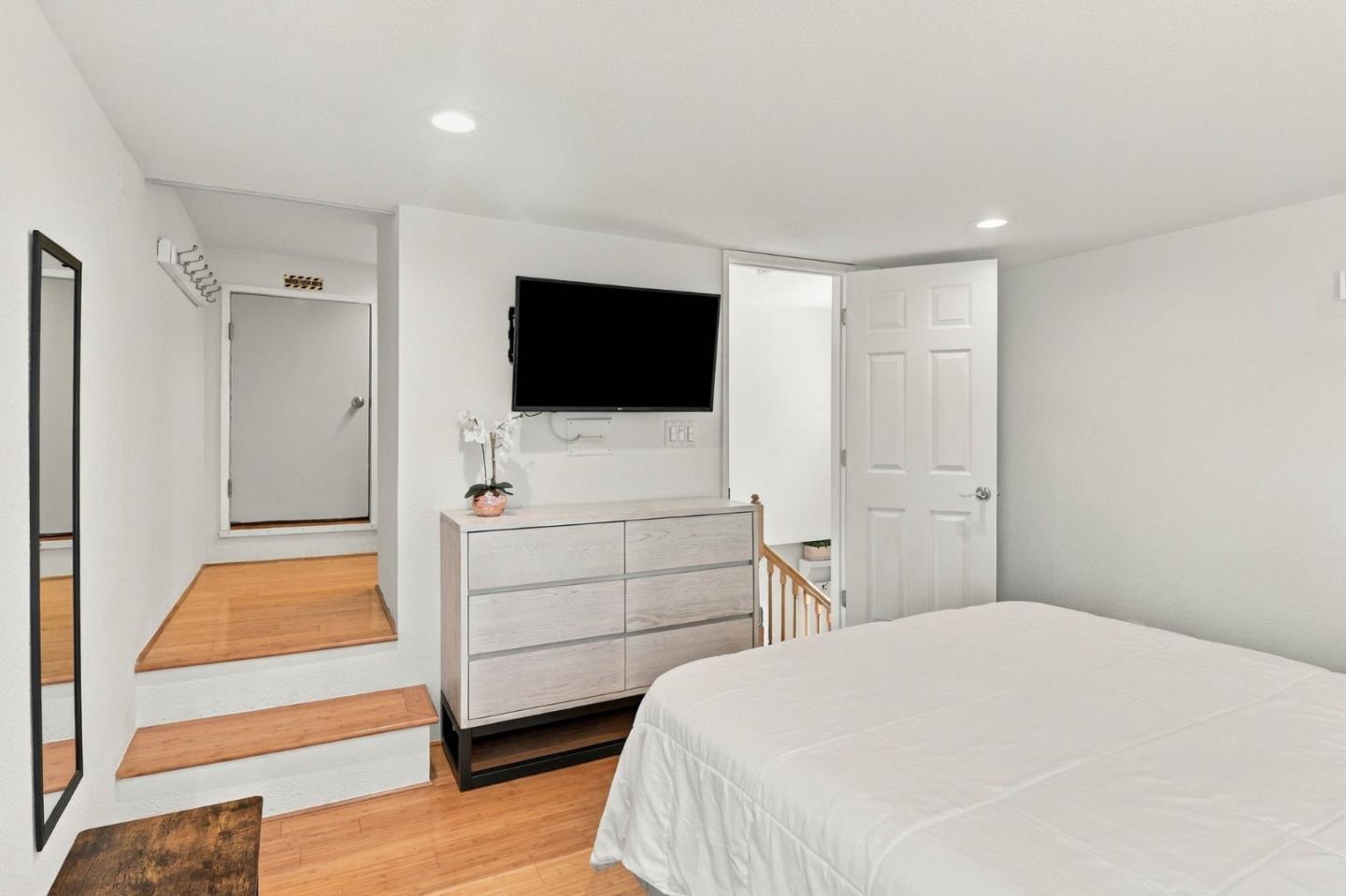 Bedroom with white bedding, wood floors, and a dresser beneath a wall-mounted television.
