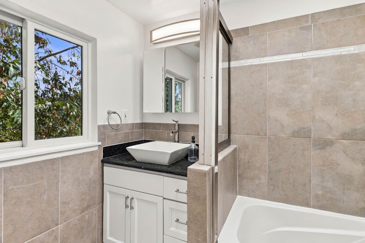Bathroom with a vessel sink vanity, tiled tub and shower, and a large window.
