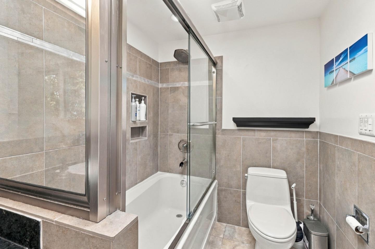 Bathroom with a glass-enclosed tub and shower, beige tile, and a toilet.