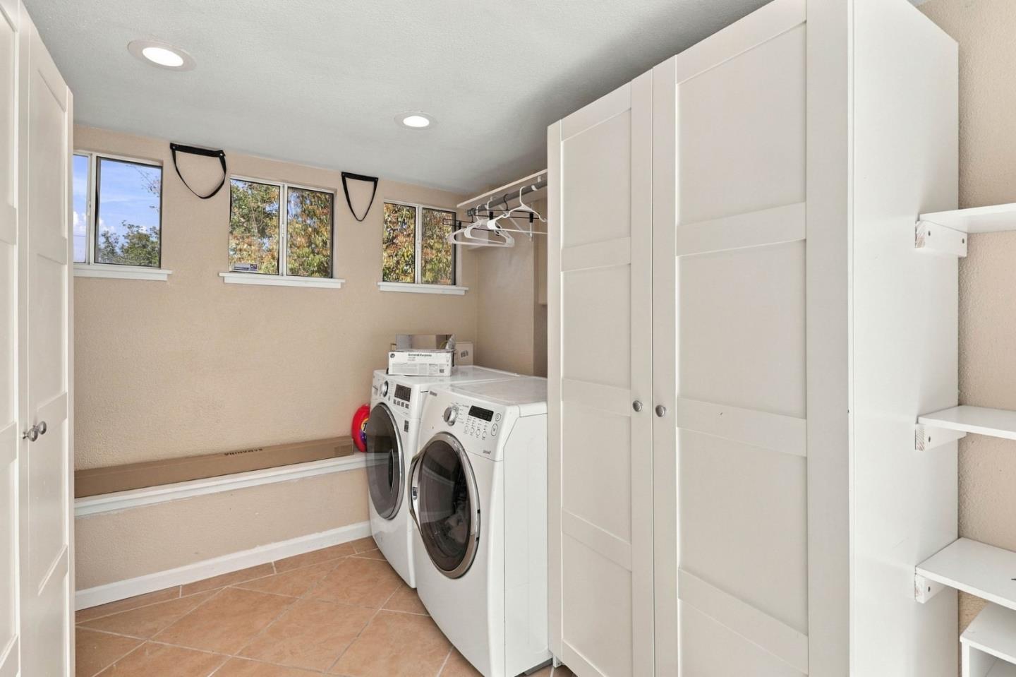 Laundry room with front-loading washer and dryer, white cabinets, and high windows.