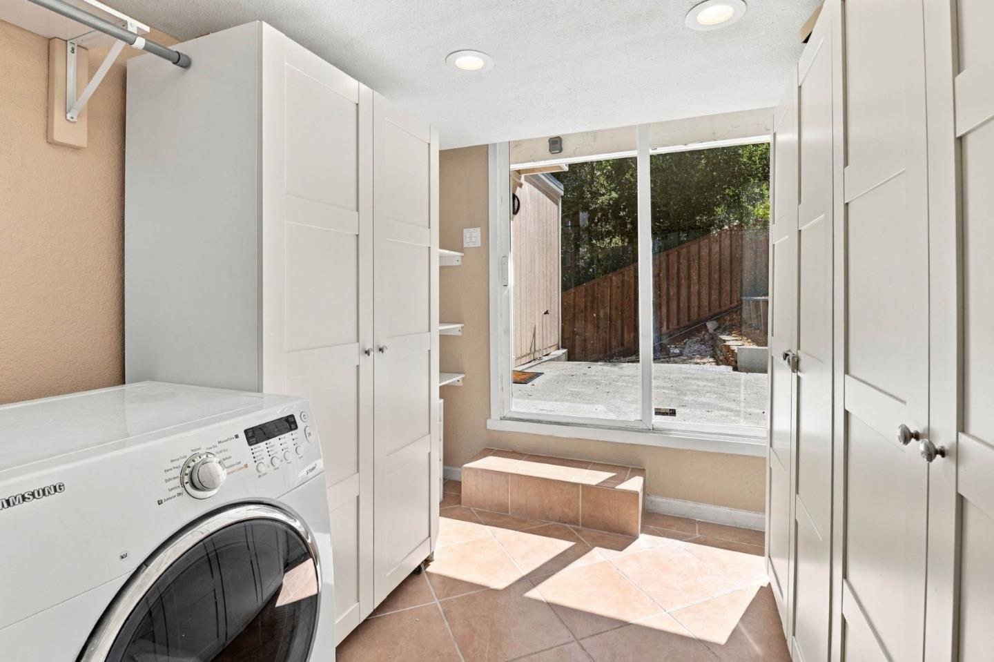 Laundry room with a front-loading washer, white cabinets, terracotta tile, and a sliding glass door to the yard.