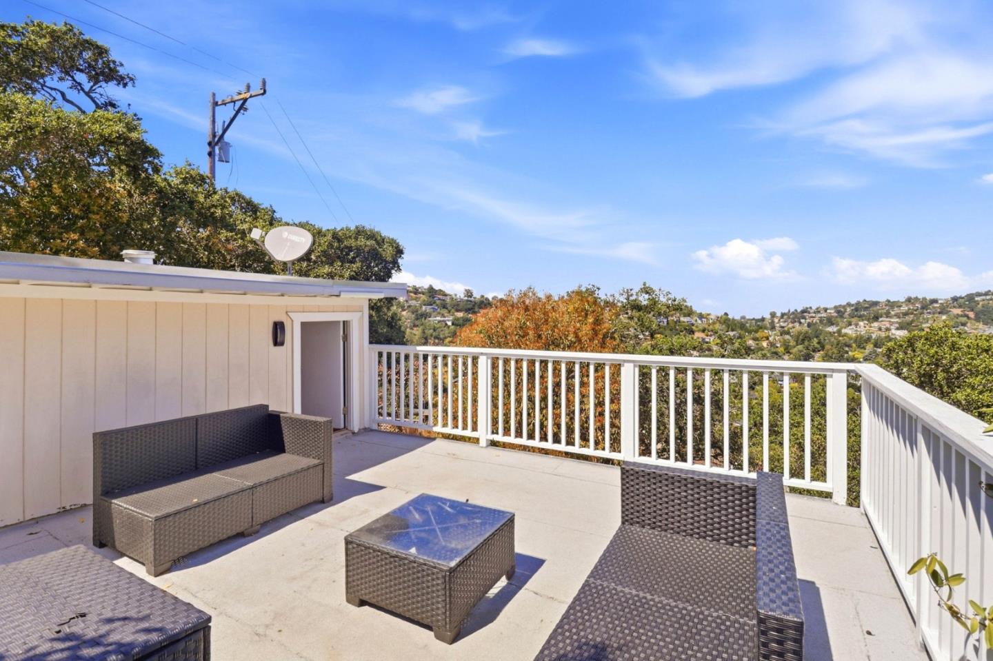 Furnished deck with white railings overlooking a green hillside neighborhood.