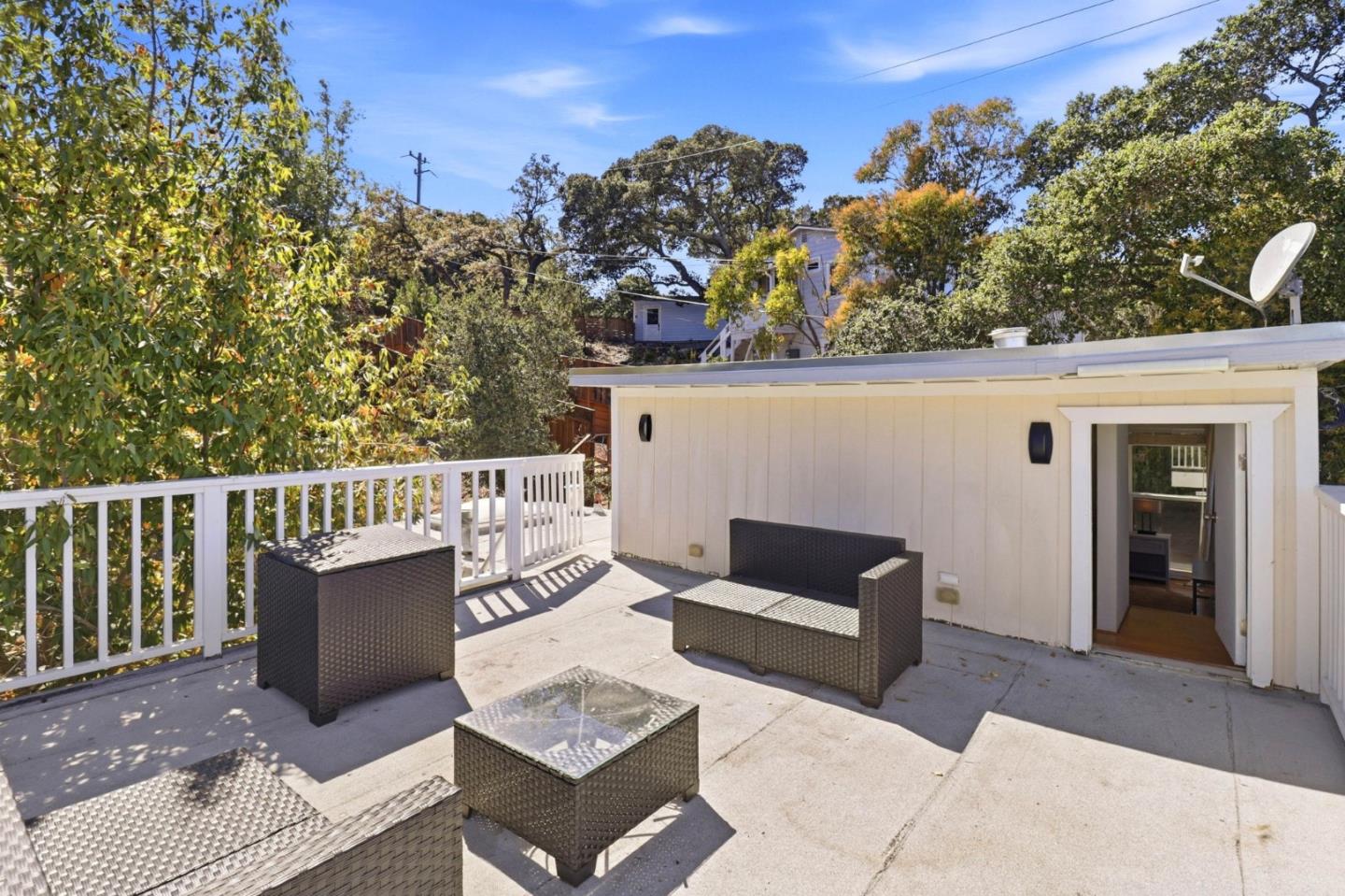 Furnished deck with woven seating, white railing, and mature trees around the home.