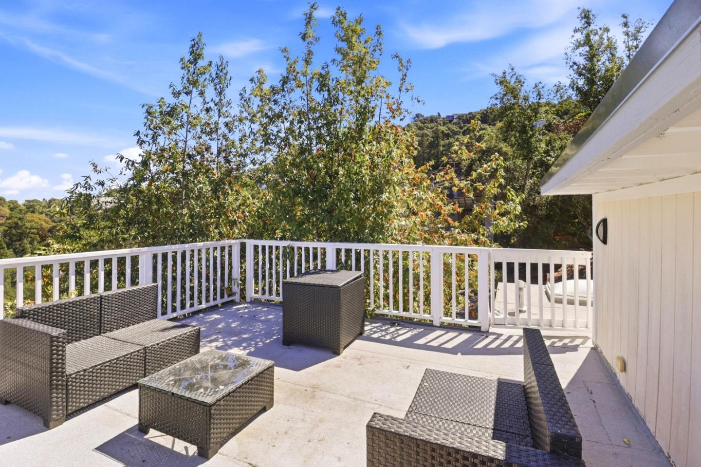 Outdoor deck with wicker seating, white railings, and leafy hillside views.