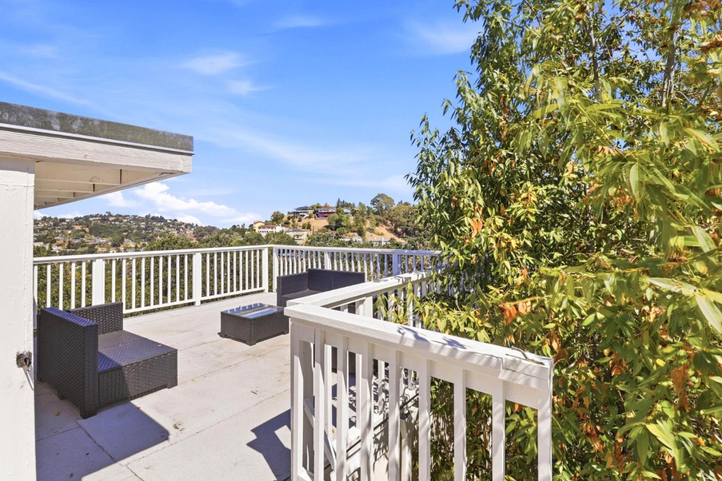 Deck with wicker seating and white railings overlooking a hilly residential neighborhood.