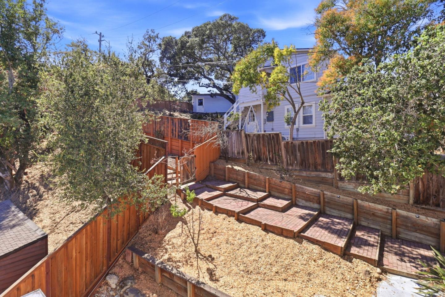Terraced backyard with brick steps, wooden fences, and mature trees behind the house.