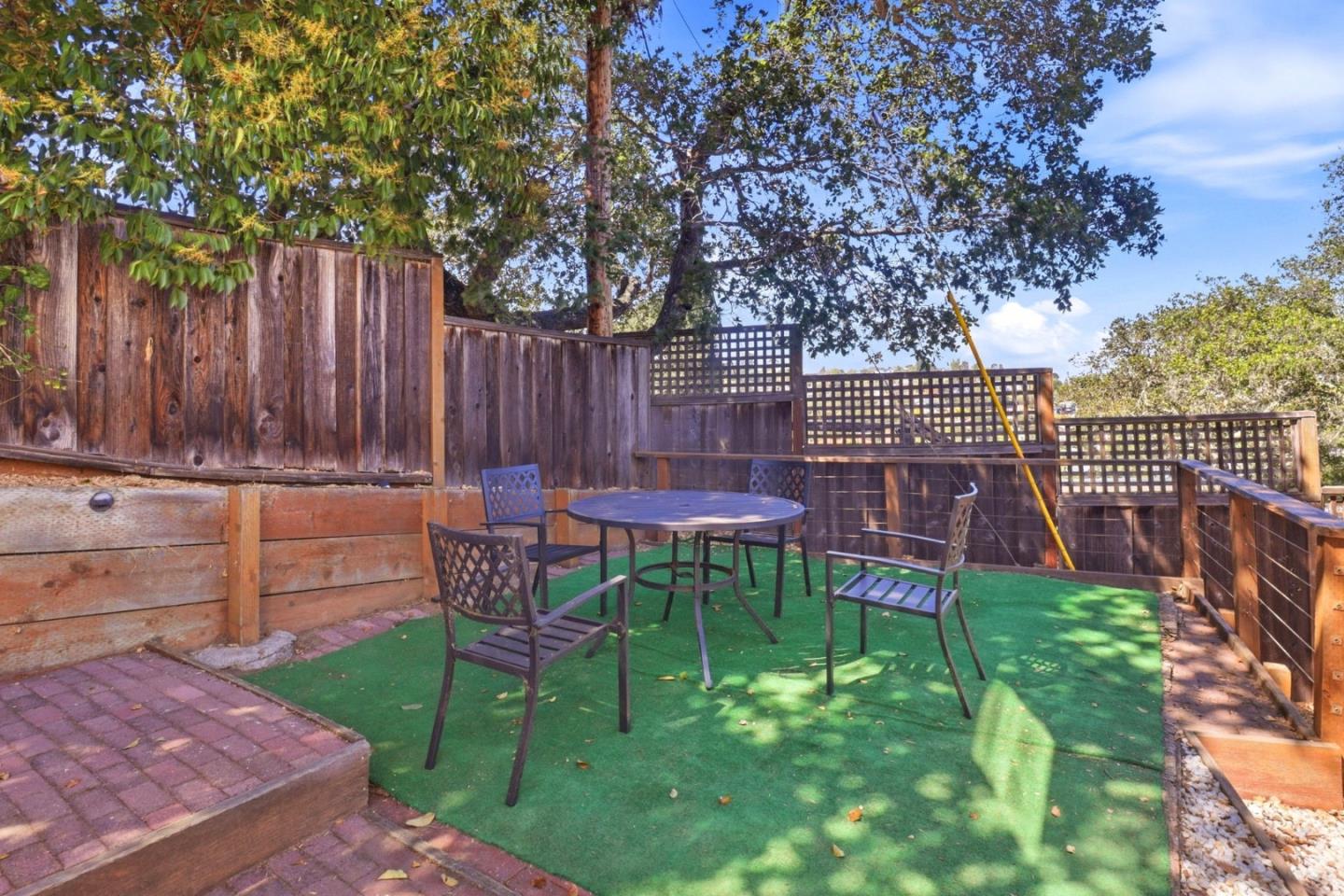 Backyard patio with a round table and chairs on green turf beneath mature trees.