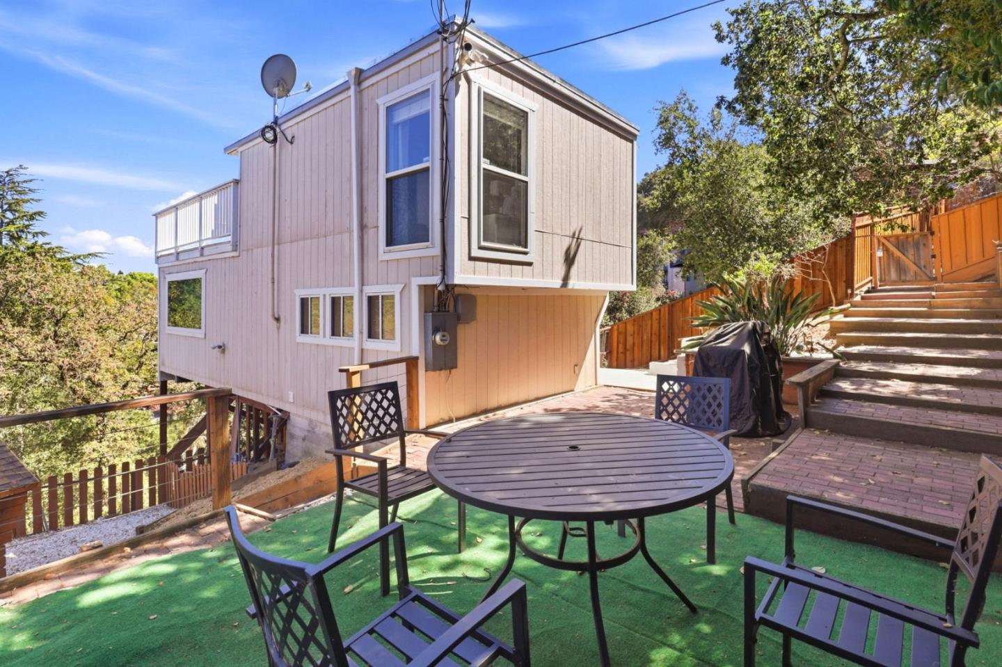 Raised two-story home beside a brick patio with outdoor dining furniture and broad steps.