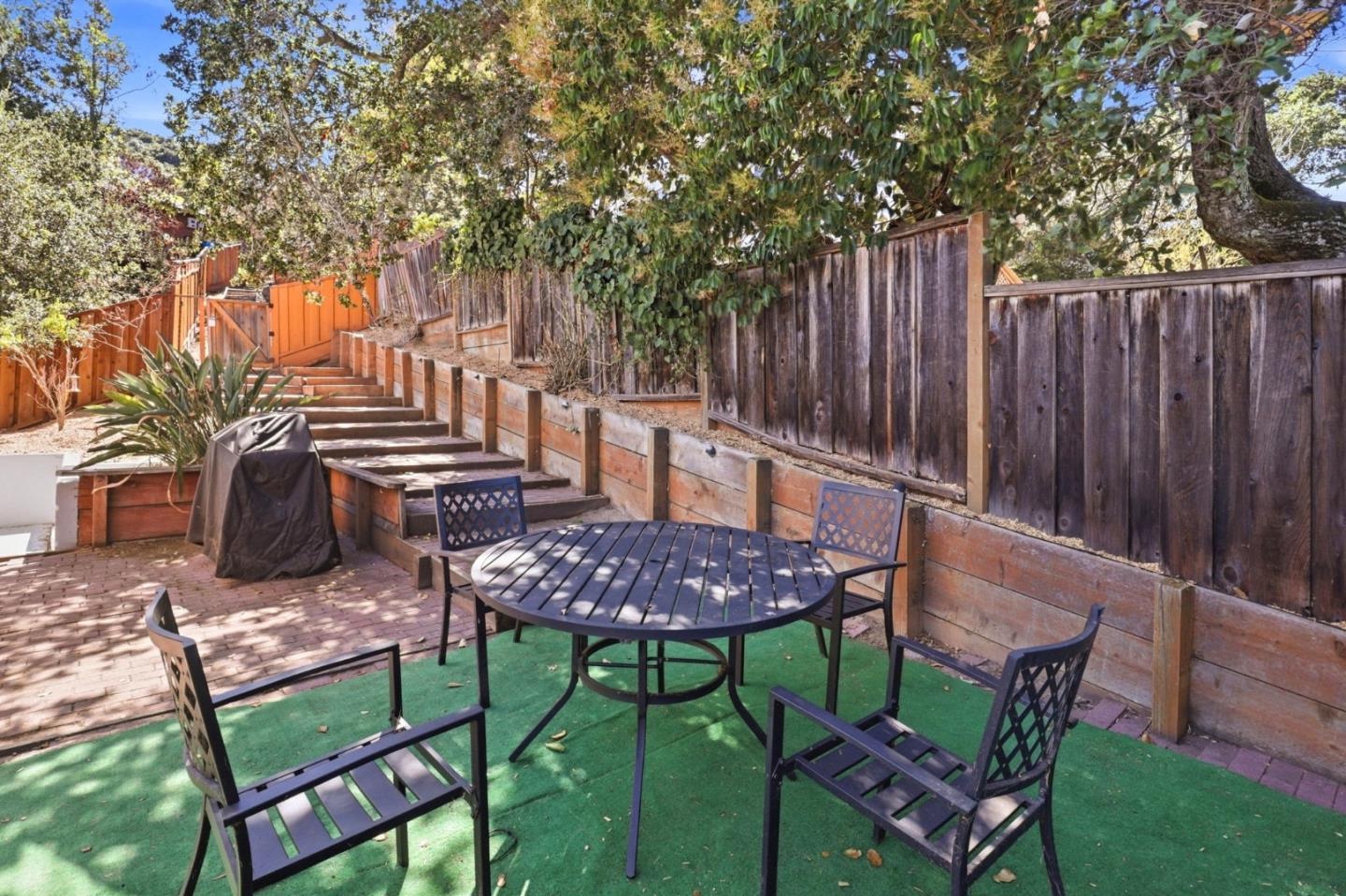 Backyard patio with a round dining table, green turf, raised planters, and tiered wooden steps.