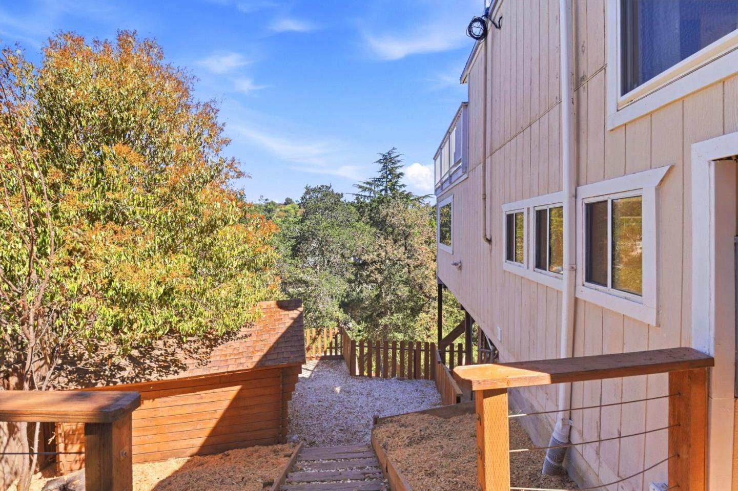 Home exterior with wooden stairs and deck railings beside autumn trees.