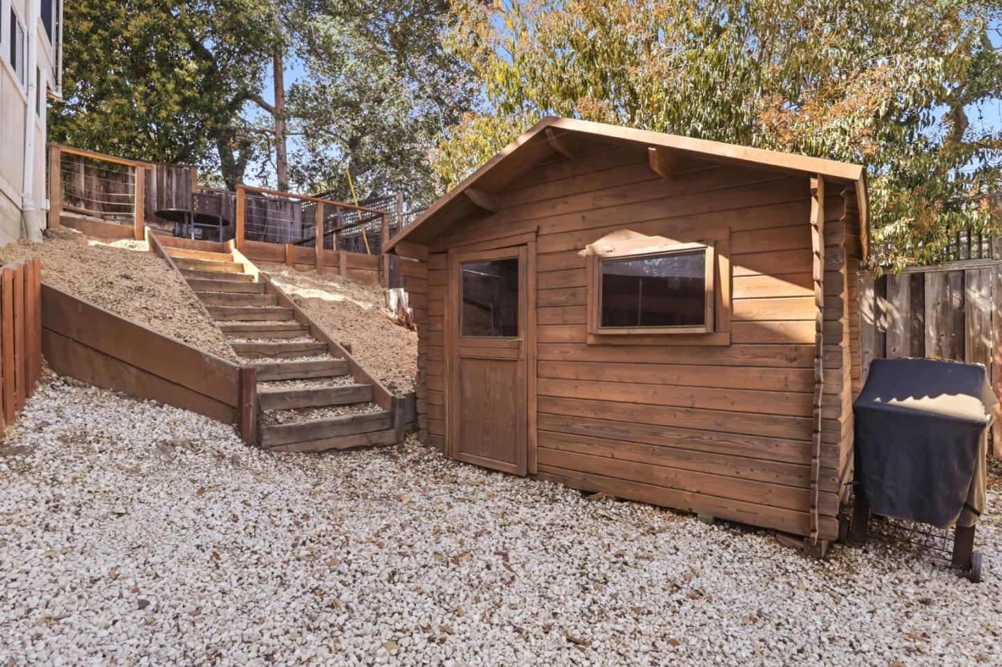 Wooden backyard shed beside gravel-covered yard and stairs leading to a raised deck.