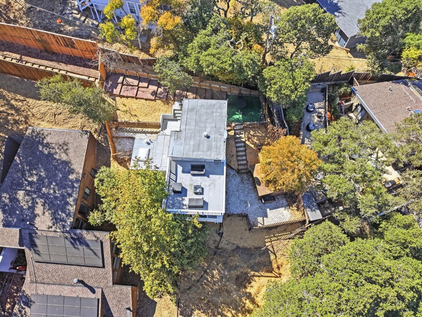 Aerial view of a home with a fenced backyard, swimming pool, patio, and mature trees.