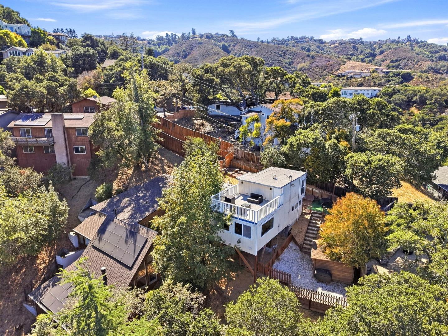 Elevated white home with a rooftop deck overlooking wooded hills and neighboring homes.