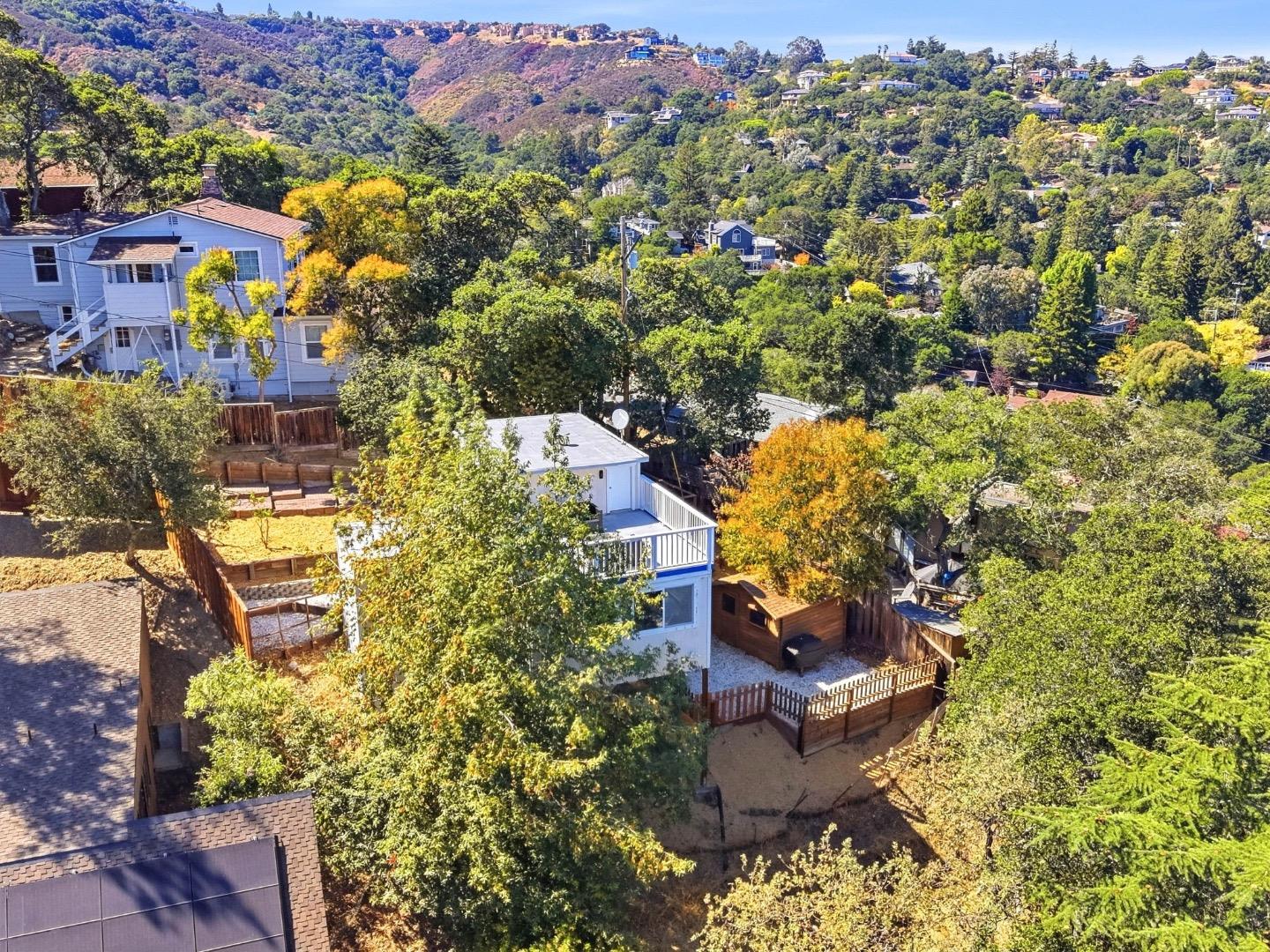 White home with a fenced backyard and deck among trees on a hillside.