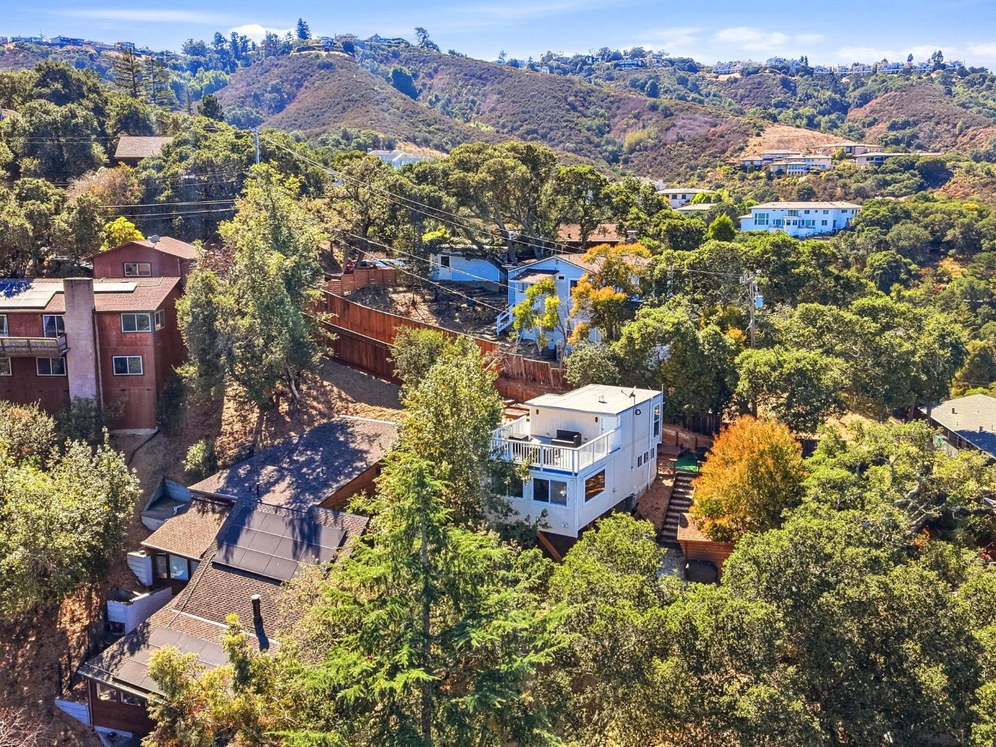 Aerial view of a white hillside home with a balcony among wooded San Carlos homes.