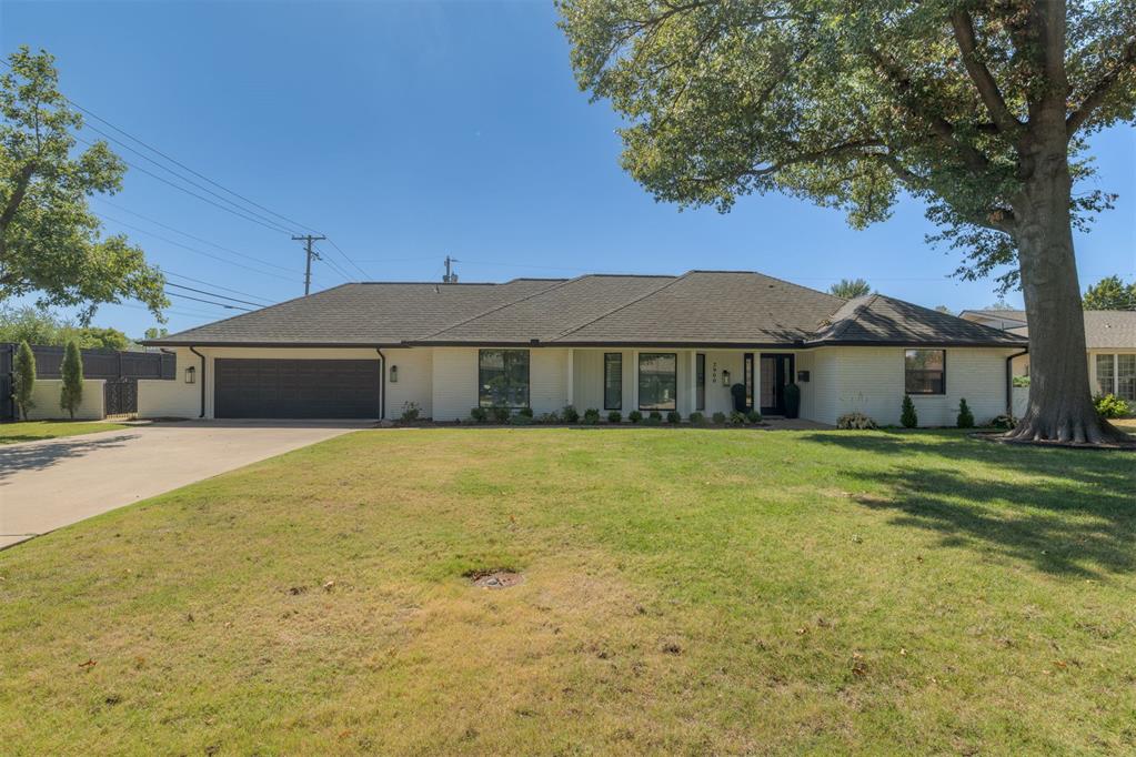 Single-story white ranch home with a dark double garage, broad driveway, and large shade tree.