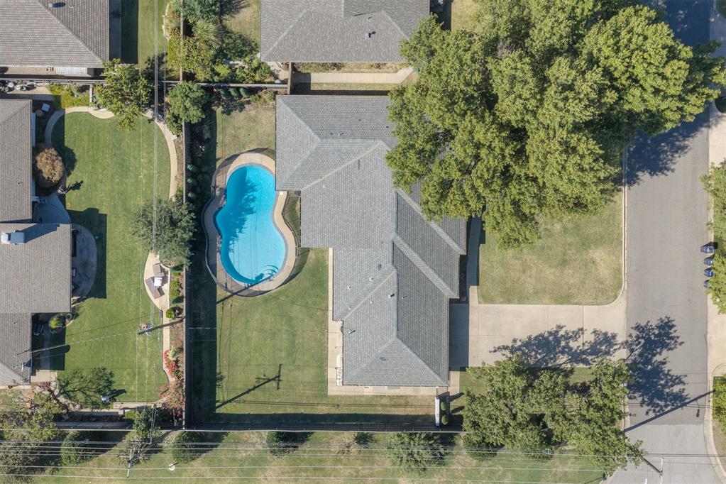 Aerial view of a home with a bright blue backyard pool, lawns, and mature trees.
