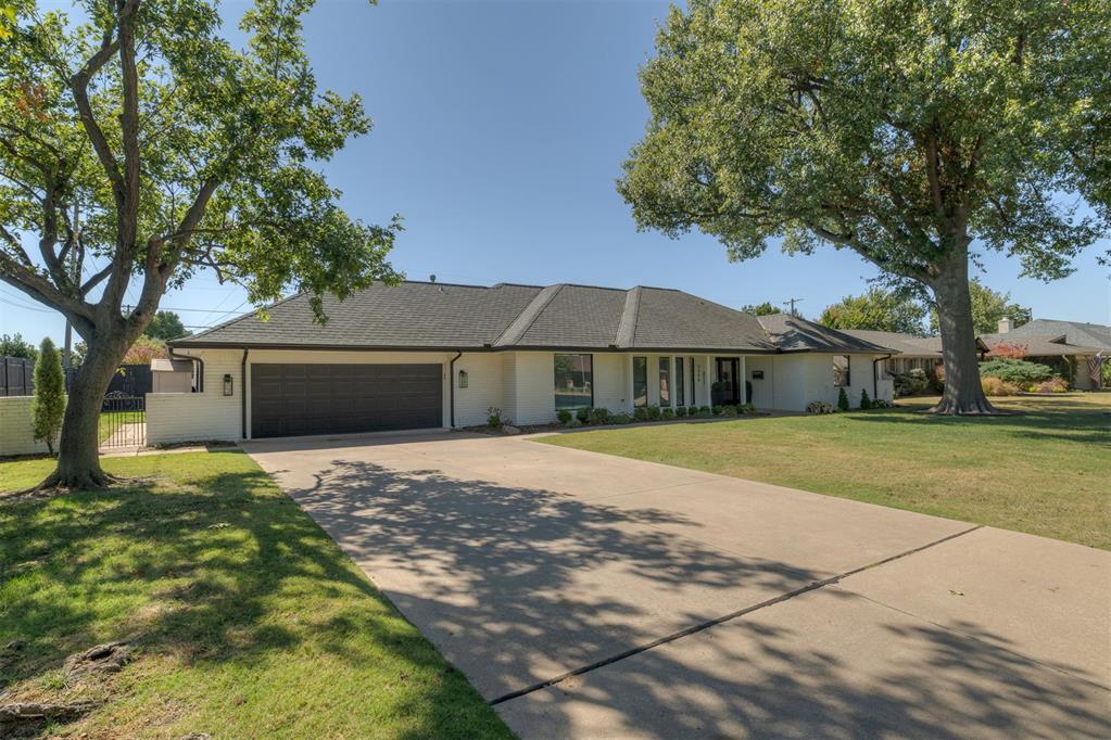 Single-story house with an attached two-car garage, broad driveway, and mature trees.