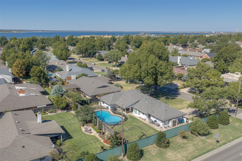 Aerial neighborhood view with a fenced backyard pool and lake on the horizon.