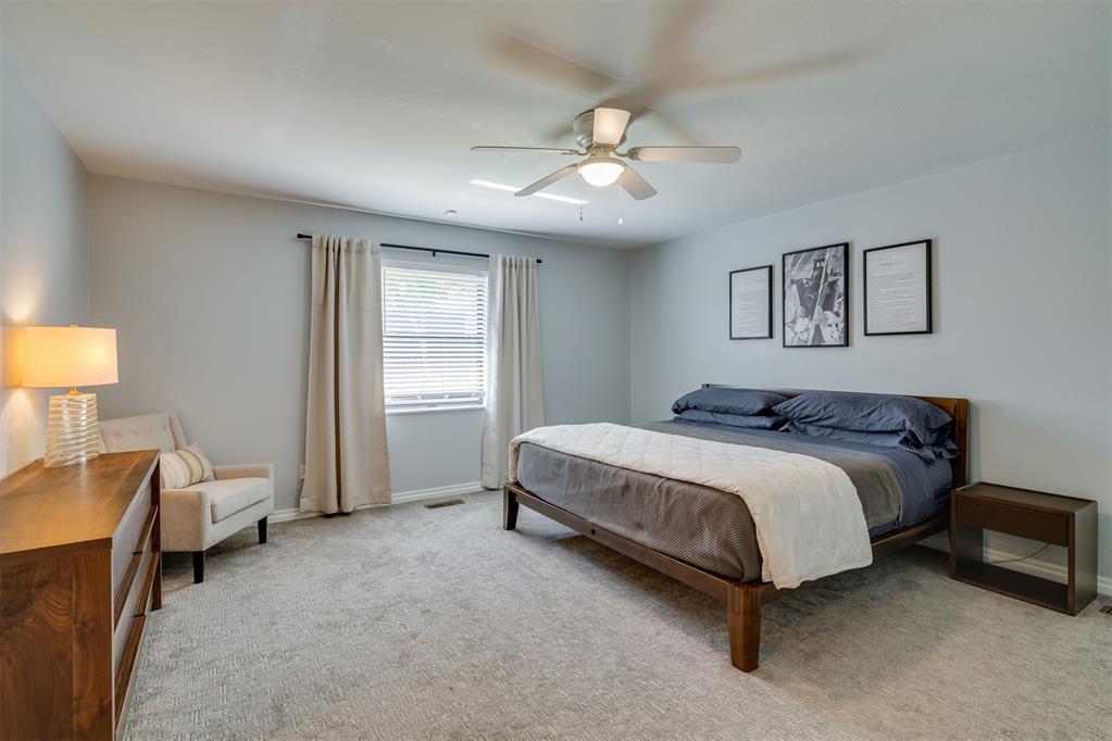 Bedroom with a dark wood bed, gray bedding, curtained window, and ceiling fan.
