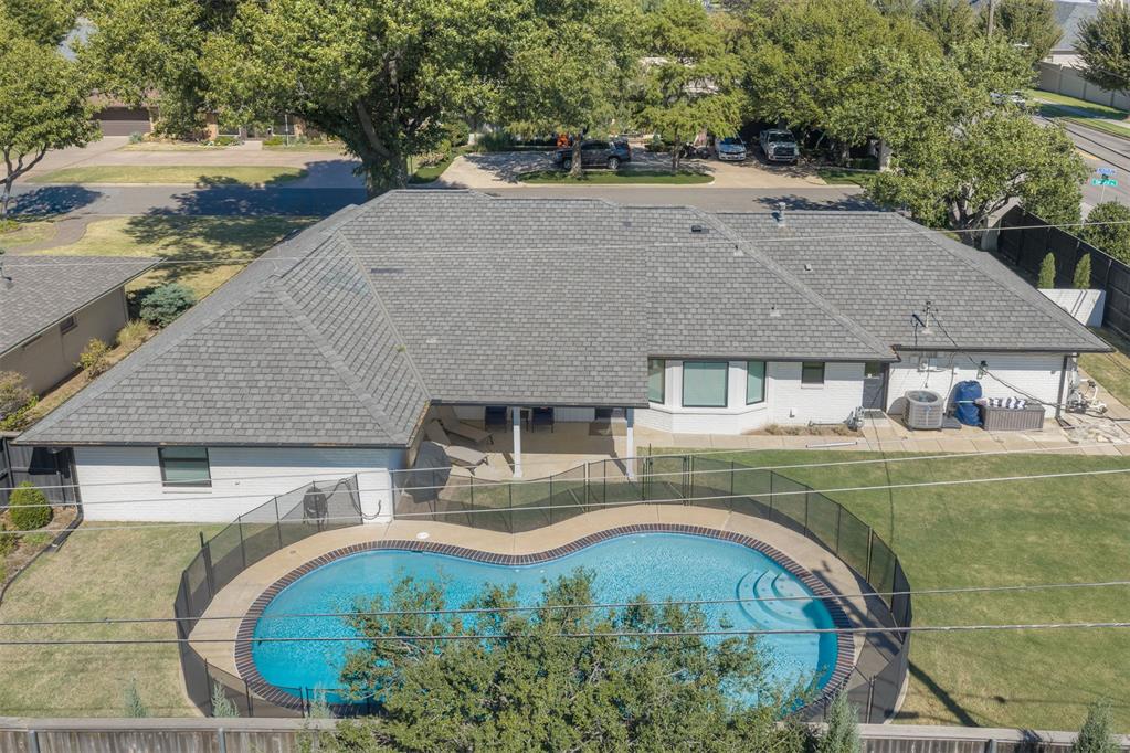 Rear of a single-story home with a covered patio and curved, fenced swimming pool.