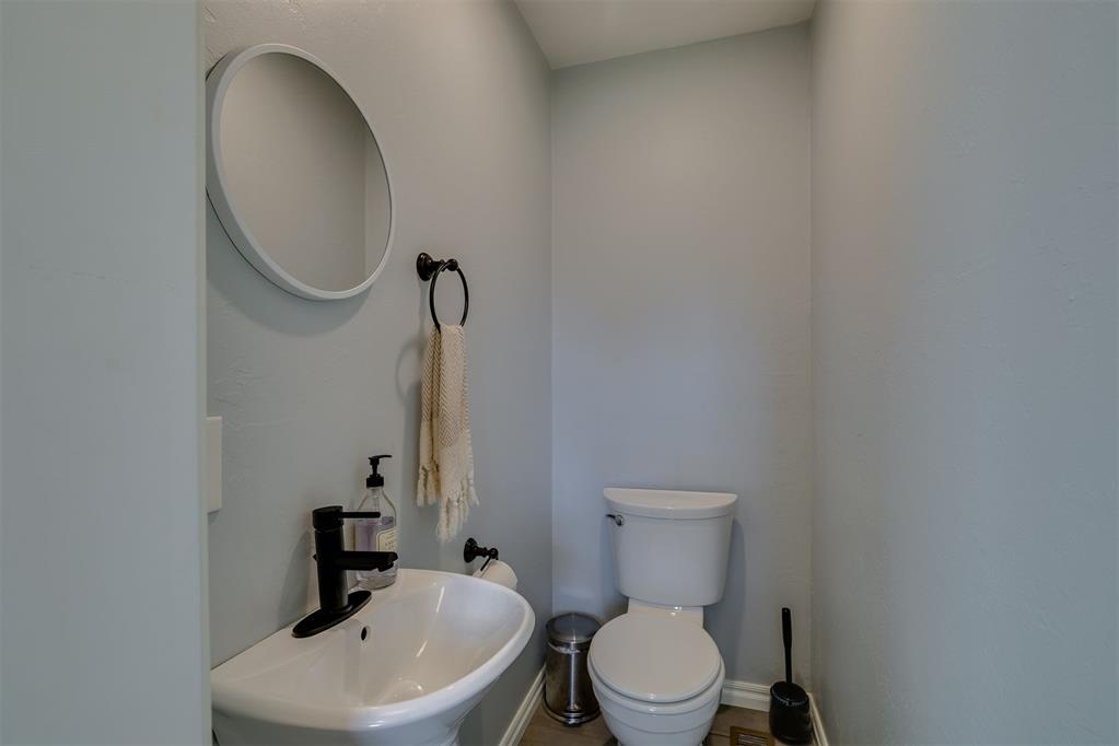 Bathroom with a pedestal sink, black faucet, oval mirror, and toilet.