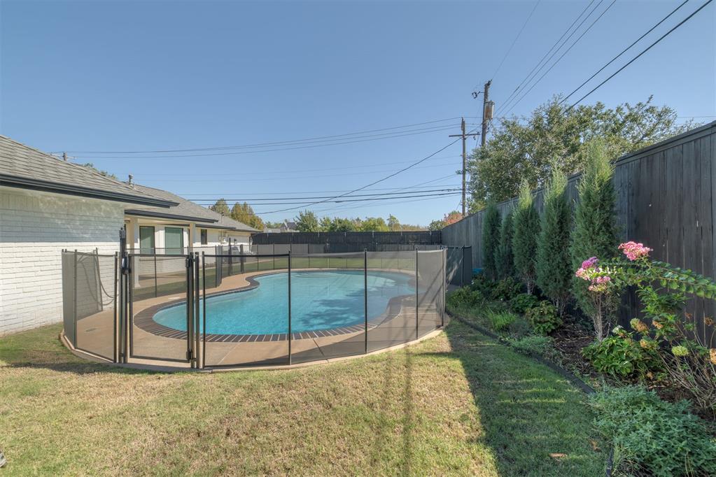 Backyard pool enclosed by a black safety fence, with a lawn and landscaped privacy border.
