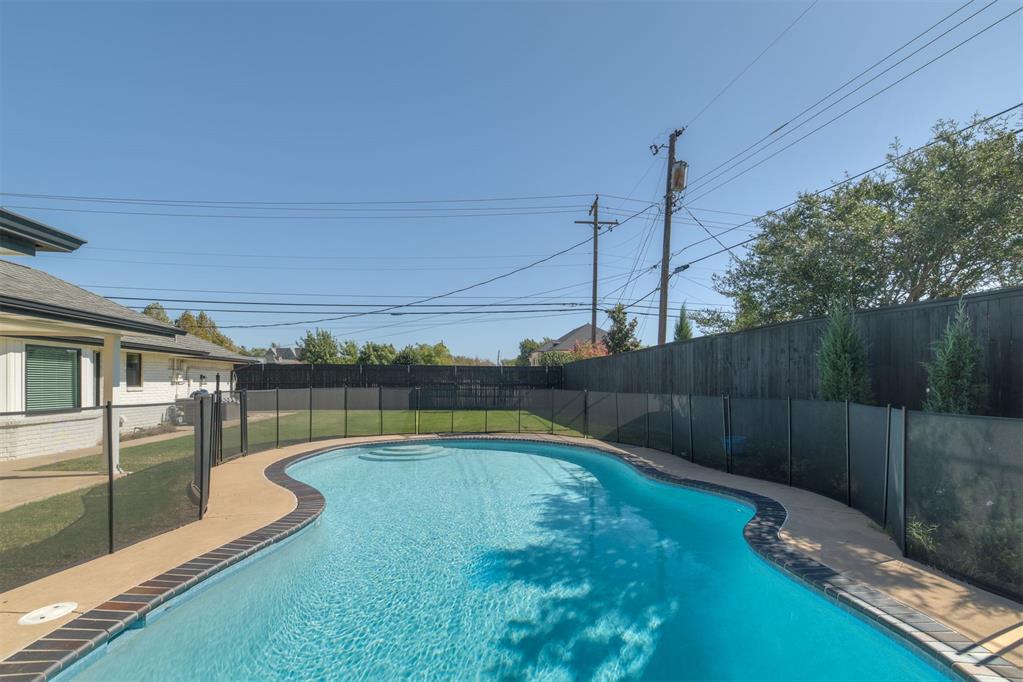Curved backyard swimming pool with a paved deck and safety fencing.