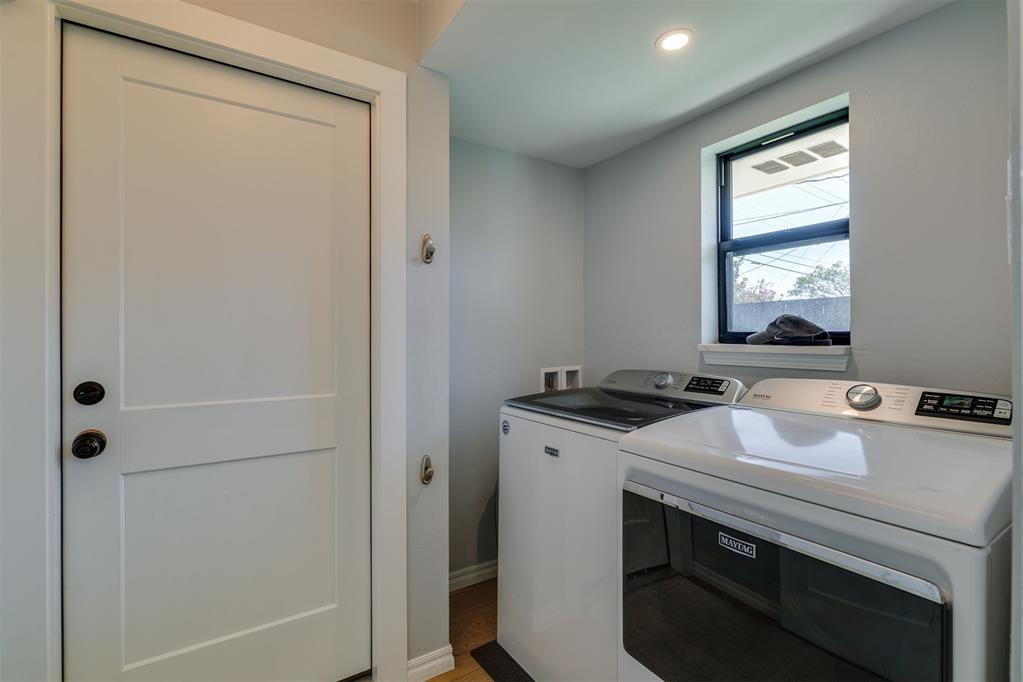 Laundry room with a front-loading washer and dryer beneath a window.