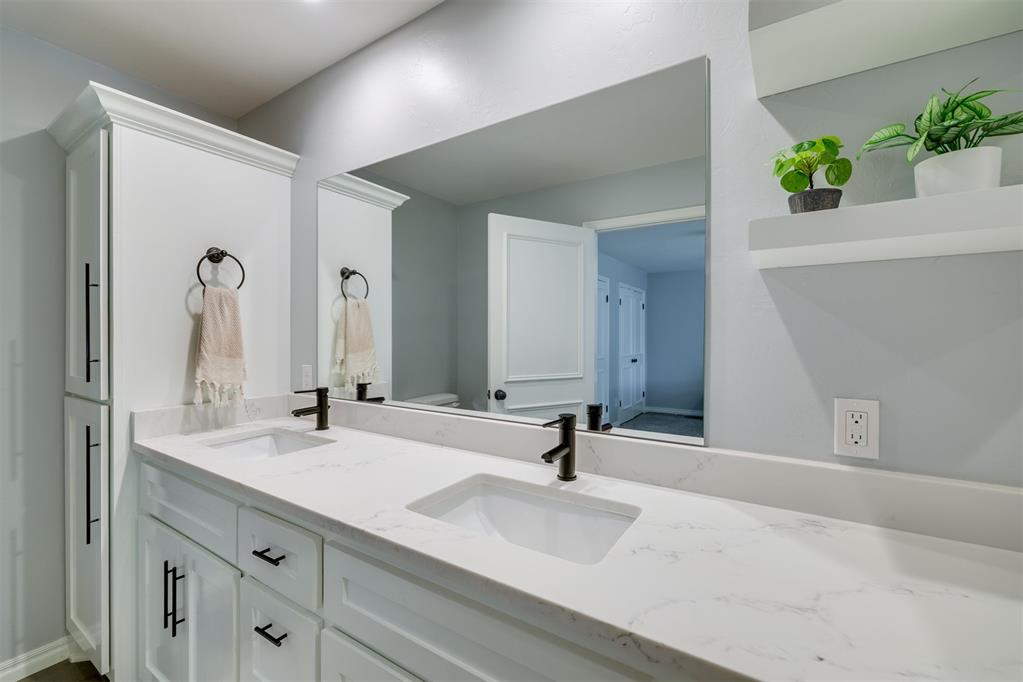 Bathroom with a long double-sink vanity, dark faucets, and a large mirror.