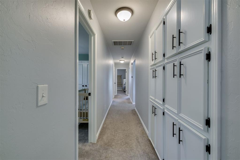 Carpeted hallway with tall white built-in cabinets and an open doorway to a room with a crib.