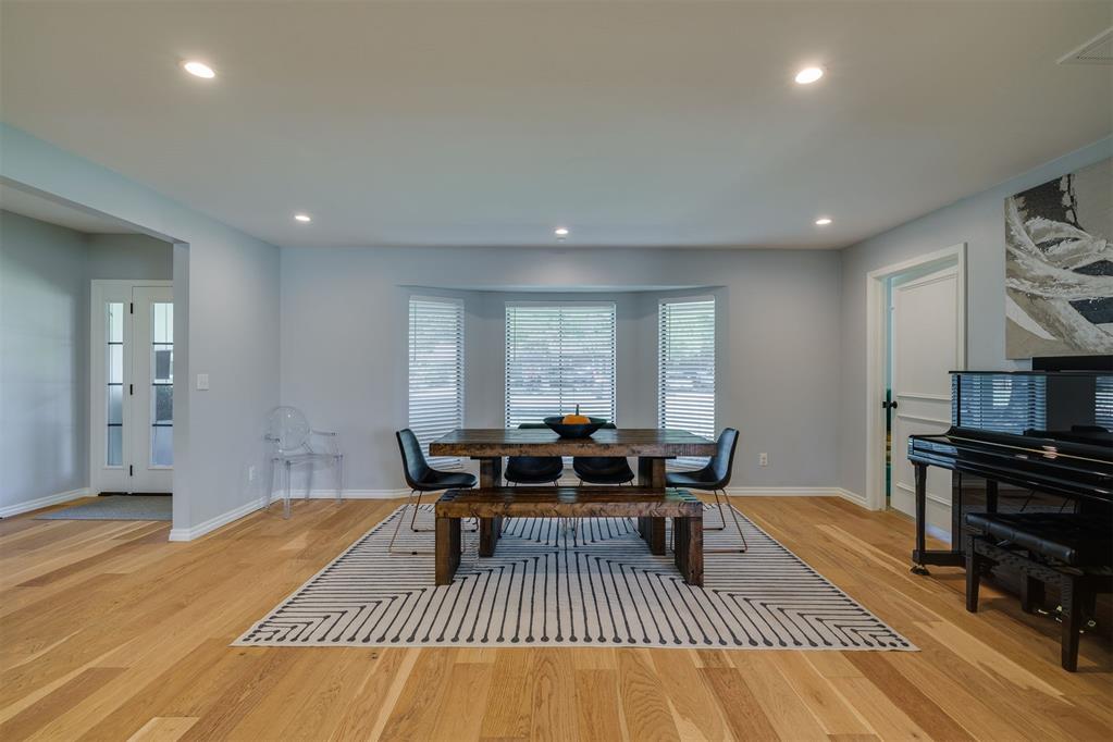 Dining room with a dark wood table, striped rug, bay windows, and black piano.