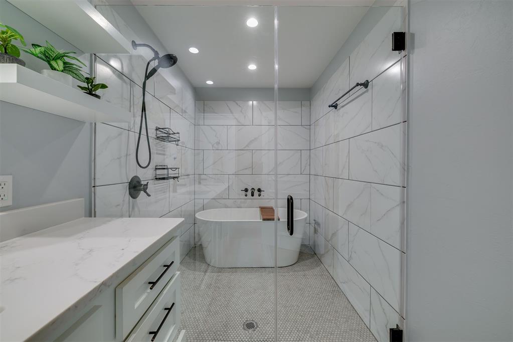 Bathroom with marble-look tile, glass-enclosed walk-in shower, freestanding tub, and white vanity.