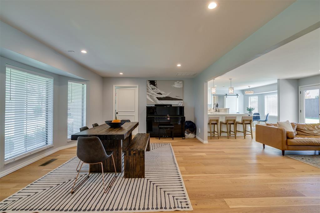 Open-plan dining and living area with a dark wood table, upright piano, kitchen island, and tan sofa.