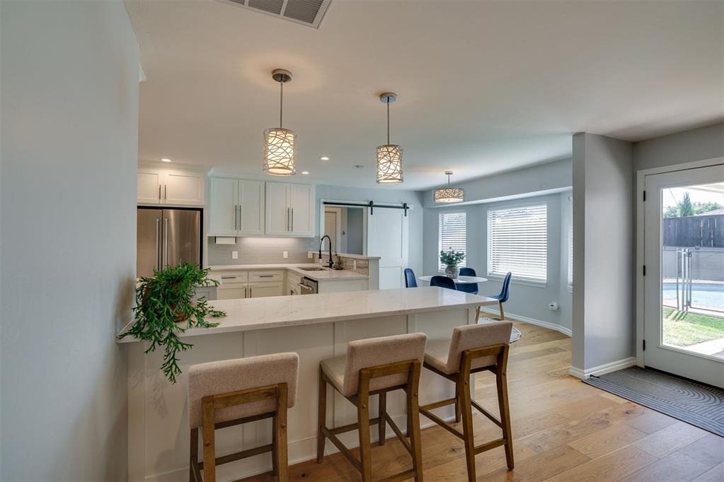 Kitchen with a large white island, three stools, pendant lights, and a pool visible through the glass door.
