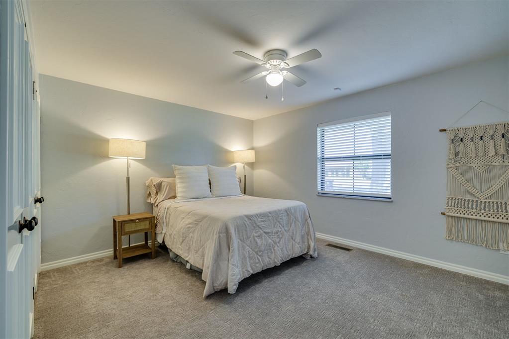 Bedroom with neutral bedding, bedside lamps, a ceiling fan, and gray carpet.