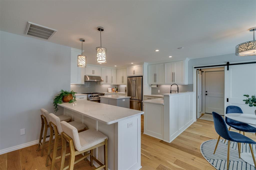 Kitchen with a large island, white cabinetry, stainless steel appliances, and blue dining chairs.