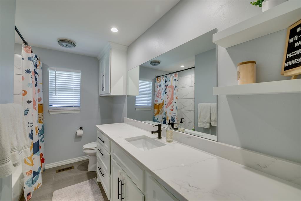 Bathroom with a long white vanity, large mirror, and colorful patterned shower curtain.