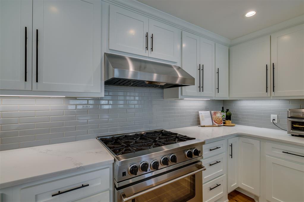 White kitchen with gray subway tile backsplash and stainless steel gas range.