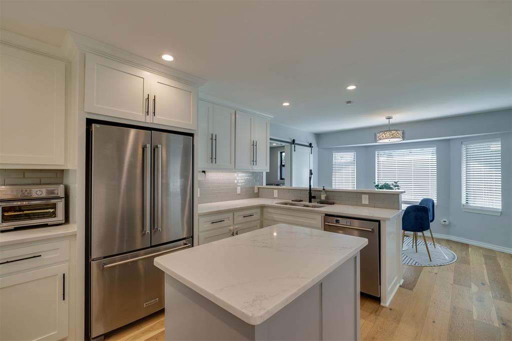 Kitchen with a large island, white cabinetry, stainless steel appliances, and a breakfast area with blue chairs.