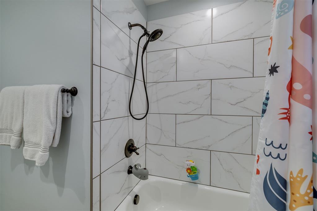 Bathroom shower and tub with marble-look tile, bronze fixtures, and colorful shower curtain.