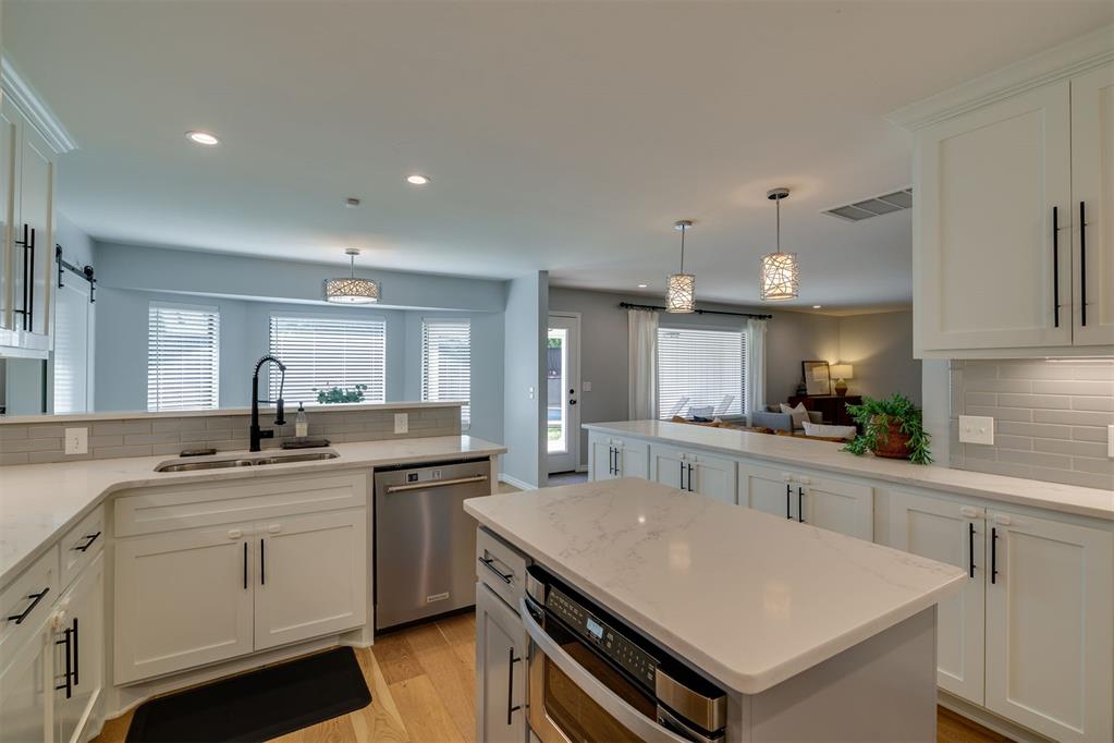 Open-plan kitchen with white cabinetry, quartz island with built-in ovens, and adjoining living area.