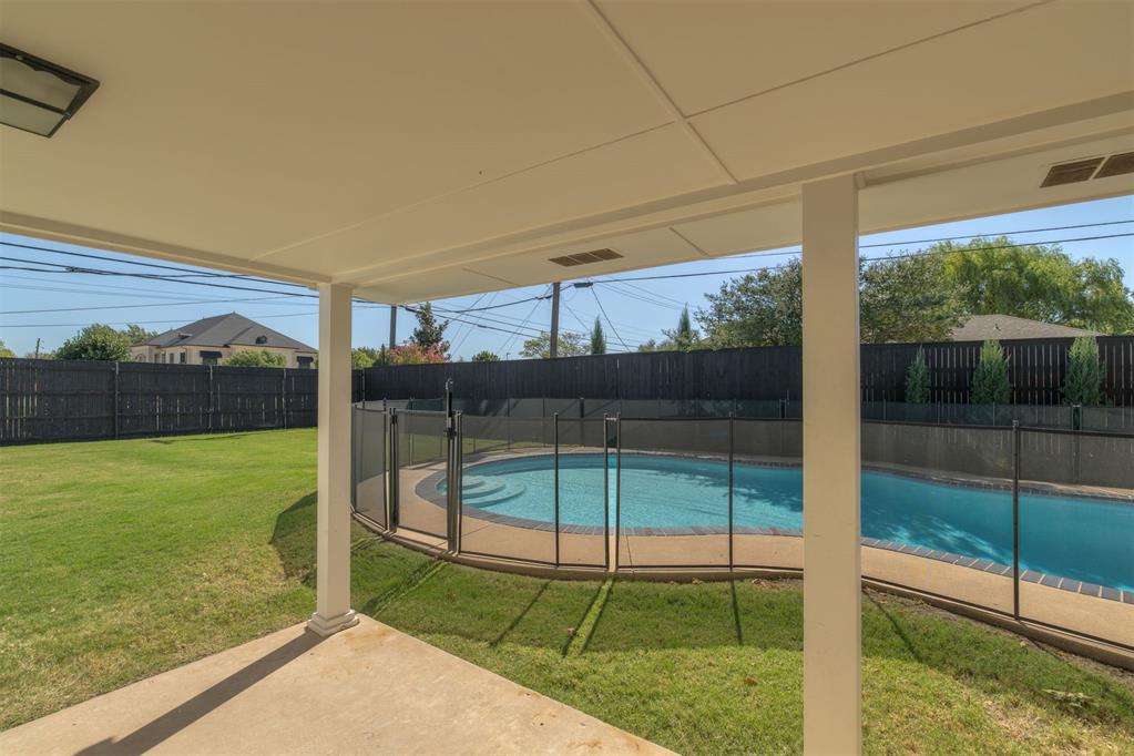 Backyard swimming pool behind a glass safety fence, viewed from a covered patio.