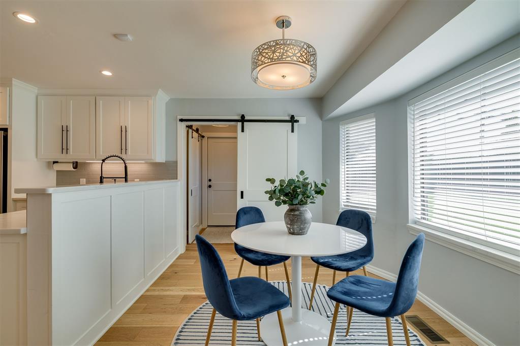 Dining area with a round white table, blue chairs, large windows, and a sliding barn door.