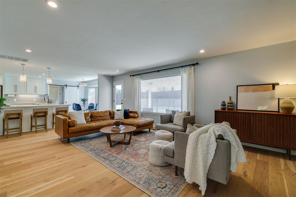 Open-plan living room with tan leather sofa, gray armchairs, patterned rug, and kitchen breakfast bar.