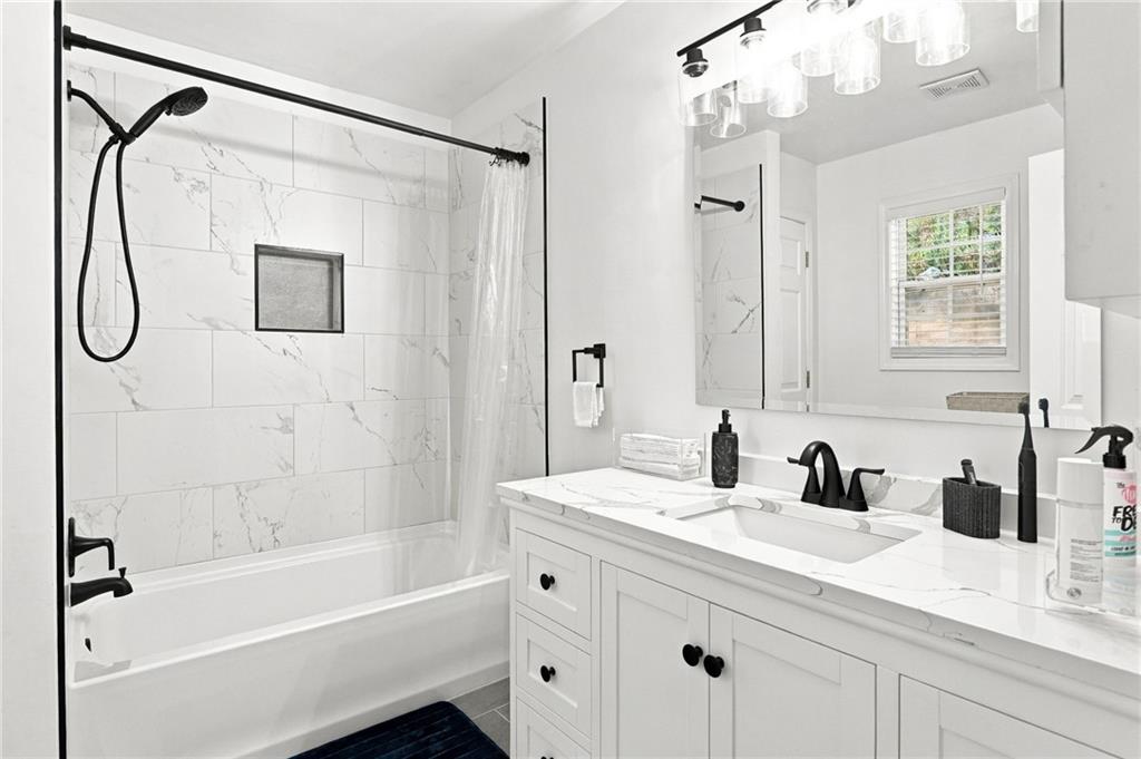 Bathroom with marble-look tub surround, black fixtures, and a long white vanity.