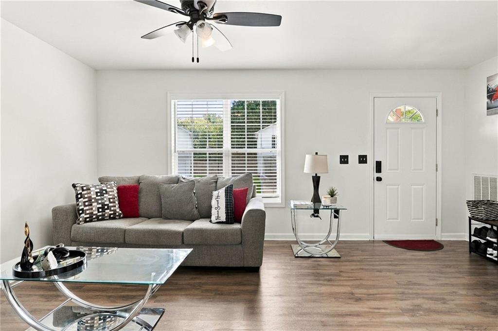 Living room with a gray sofa, glass coffee table, ceiling fan, and white front door.